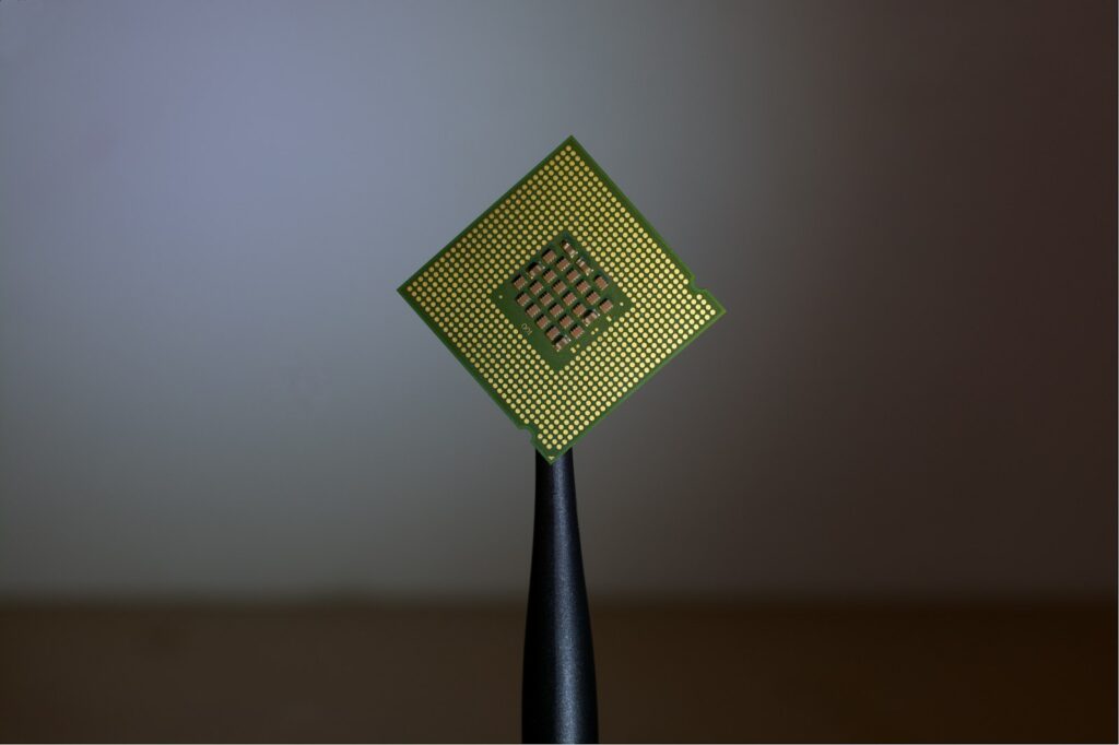 A computer processor held by black tweezers above a circuit board