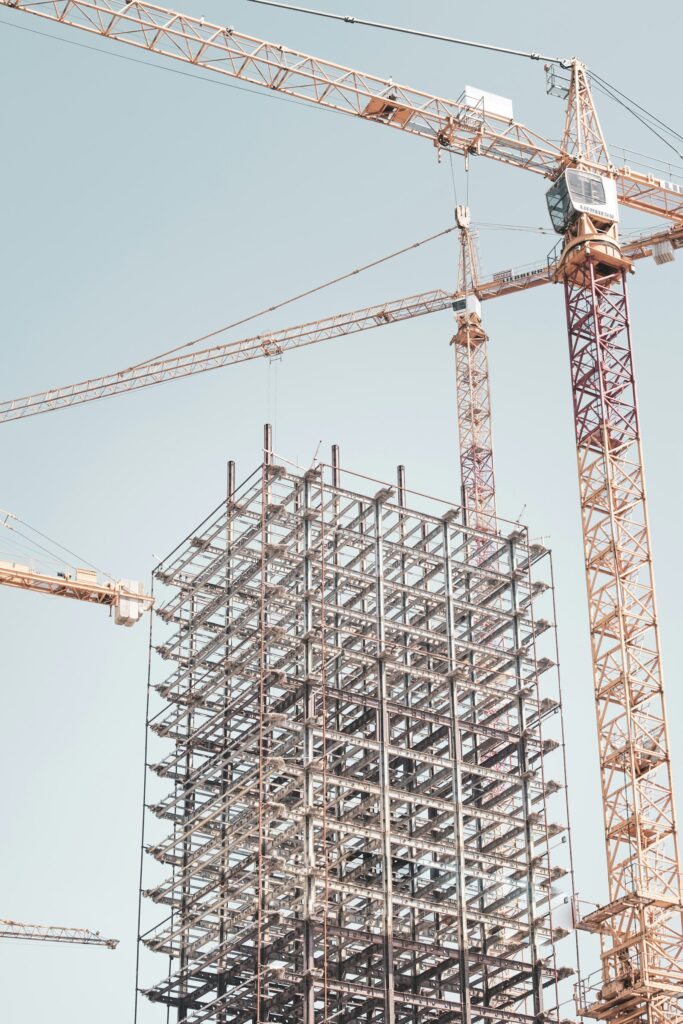 A gray metal building frame beside a tower crane on a construction site