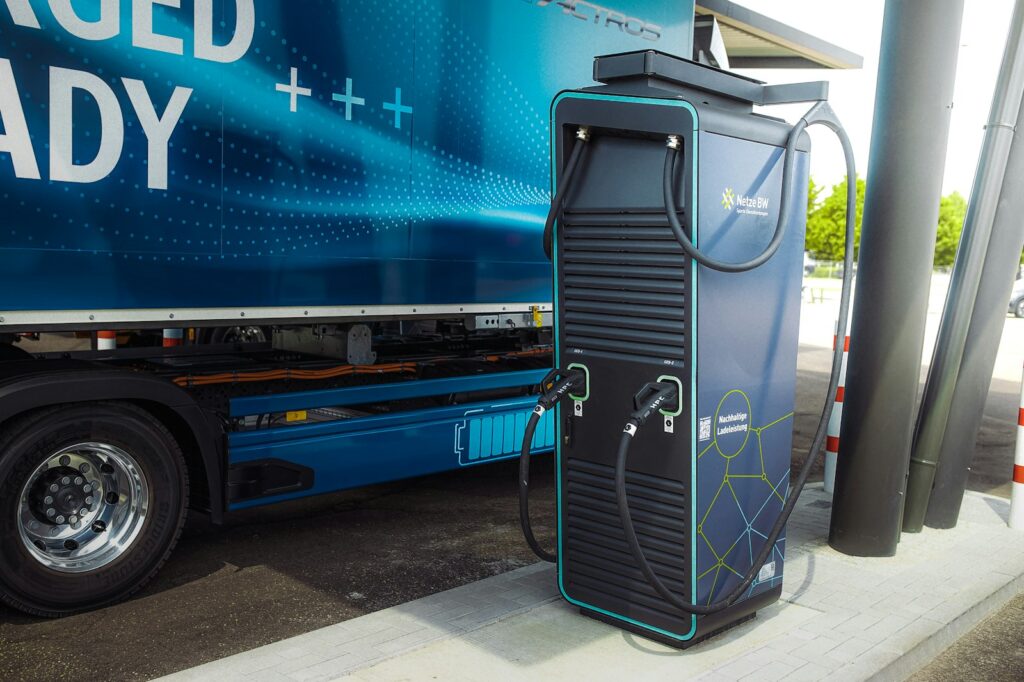 An electric truck parked at a charging point with its door open