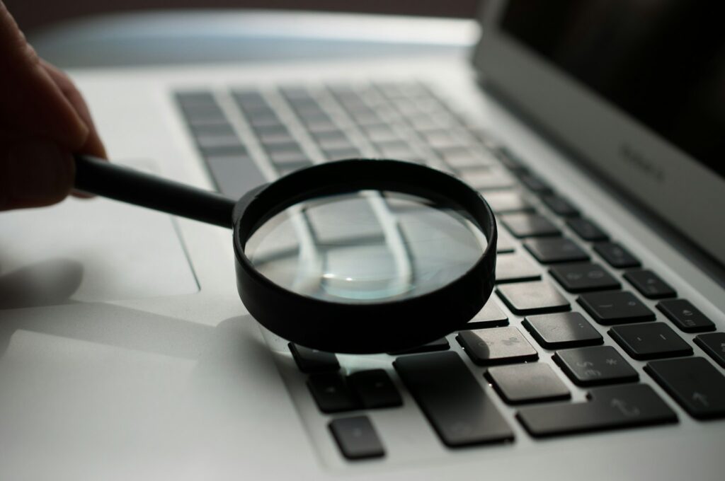 A magnifying glass lying next to a gray laptop computer
