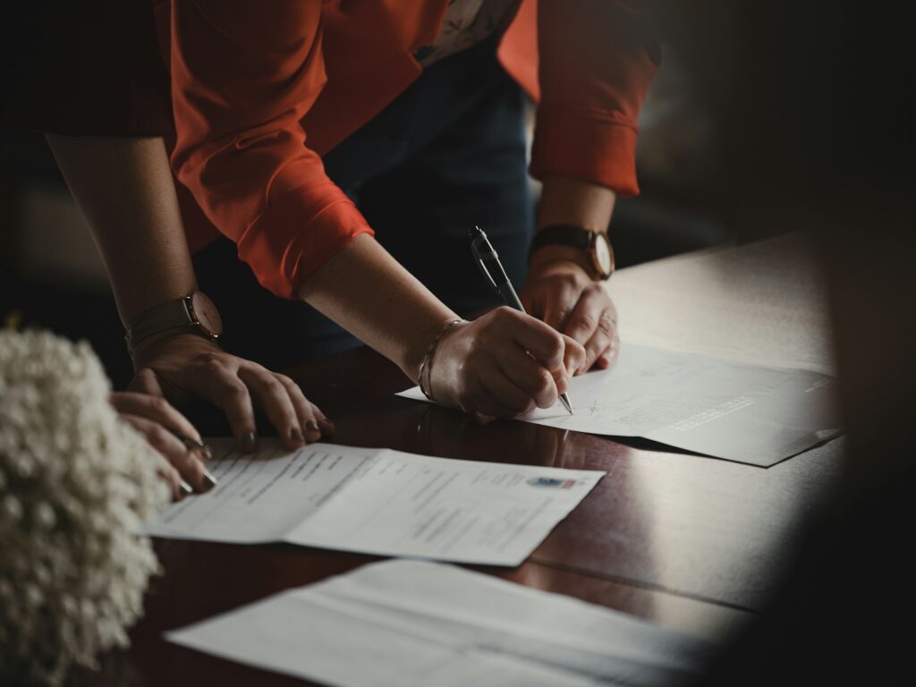 A person in an orange long sleeve shirt writing on paperwork at a desk