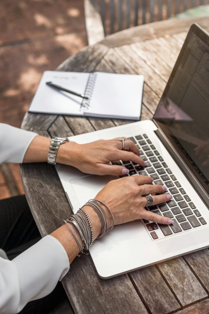 A person typing on a laptop on a brown wooden desk